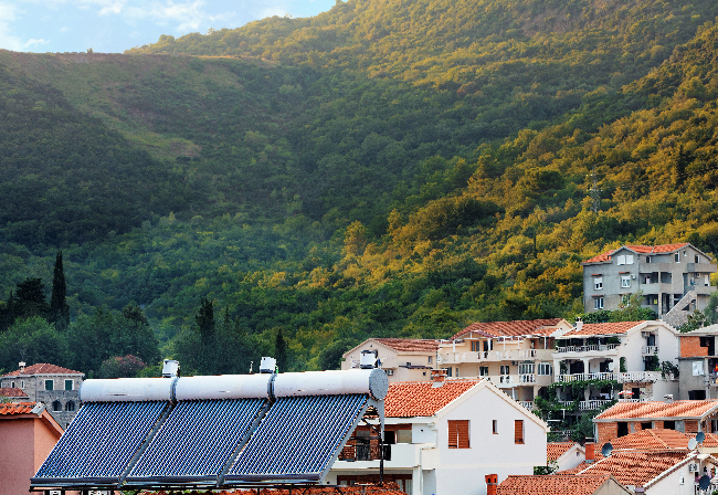 solar water heaters on orange tile roof of house against background of a mountain landscape in Montenegro