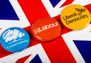 Union jack flag with 3 badges for the Tory, Labour and Lib dem parties.