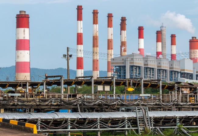 Daytime shot of an Asian coalfired plant, with several red and white high chimneys and industrial metalwork in the foreground