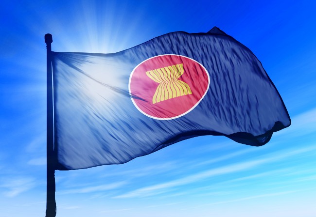 Close-up of ASEAN flag, yellow emblem on red circle on dark blue background. Flag fluttering in the wind with sun shining behind.